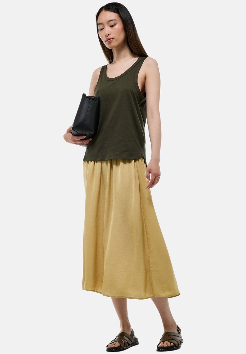 Débardeur vert olive, jupe maxi jaune, sac noir. Sandales avec des brides et semelle texturée. Tissu doux, coupe décontractée, design superposé.