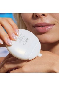 Vit cirkulär kosmetisk behållare som hålls i handen, med kräm som pressas ut på huden. Slät yta, minimalistisk design och produktetikett synlig.