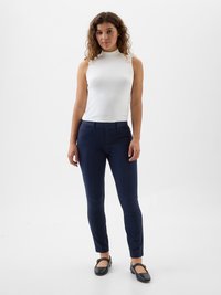 White sleeveless top, navy slim-fit pants, smooth texture, minimal design, flat black shoes. Model poses against a plain white background.