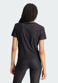 Fekete, rövid ujjú póló texturált geometriai mintával, karcsúsított szabással és kerek kivágással, párosítva hozzá illeszkedő, magas derekú leggingssel.