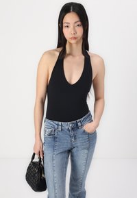 Fekete, hát nélküli fürdőruha mély V-kivágással, amelyet közepes derekú kék farmernadrággal párosítanak. A modell egy fekete, steppelt kézitáskát tart.