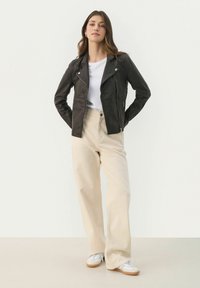 Giubbotto da biker in pelle nera con zip asimmetrica, abbinato a pantaloni a gamba larga crema e sneakers bianche. Sotto una semplice t-shirt bianca.