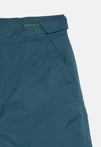 Mėlynos izoliacinės kelnės su lygiu paviršiumi, turinčios elastingą liemenį, velcro užsegimą ir šonines kišenes.