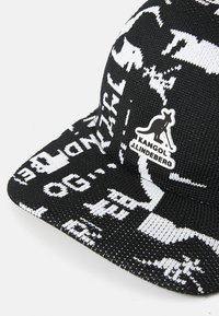 Gorra negra con patrones gráficos y texto en blanco. Hecha de tela texturizada, presenta una etiqueta con el logo de Kangol y J.Lindeberg en la parte delantera.