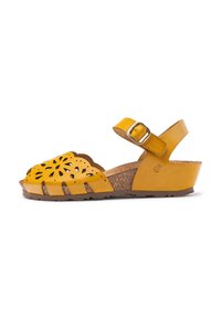 Yellow leather sandal with laser-cut floral design, adjustable ankle strap, cork sole, and a wedge heel. Round, open-toe shape.