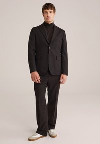 Costum negru ajustat cu un guler înalt asortat, purtat cu adidași albi. Material fin, croială slim, rever cu crestătură și buzunare laterale.