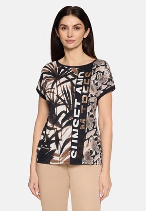 Frau trägt ein kurzärmeliges Oberteil mit gemischten abstrakten Mustern und dem Text "Sunset and antidesc" in Schwarz-, Braun- und Beigetönen.