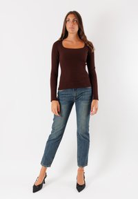 Maglietta marrone a maniche lunghe con scollo quadrato, abbinata a jeans dritti blu chiaro e tacchi neri a punta.