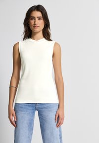 Top blanco sin mangas con un cuello alto, hecho de una tela suave. Combinado con unos vaqueros de mezclilla azul claro, que tienen un corte relajado y pierna recta.