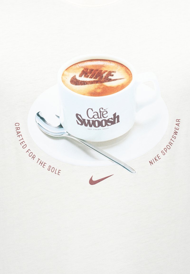 Tazza e piattino da caffè bianchi con cucchiaino, schiuma di caffè che mostra il logo "Nike", testo intorno che recita "Realizzato per la suola" e "Nike sportswear."