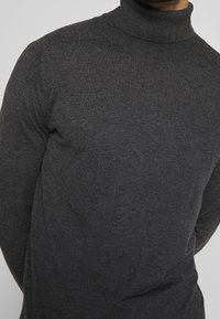 Dunkelgrauer Rollkragenpullover aus weichem, strukturiertem Strick. Hat ein figurbetontes Design mit gerippten Details am Kragen und an den Bündchen.