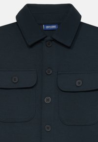Camicia blu scuro con colletto, realizzata in un tessuto testurizzato, sei bottoni neri e due tasche sul petto. L'etichetta riporta "ONLY & SONS."