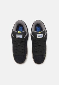 Schwarze Wildleder-Sneaker mit schwarzen Schnürsenkeln, grauem Futter und grünen Ziernähten; ausgestattet mit einer gepolsterten Zunge und einer strukturierten Gummisohle.