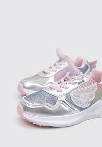 Zapatillas deportivas plateadas con acentos iridiscentes, cordones rosas y detalles decorativos en forma de alas en los costados. Material texturizado.