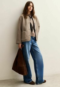 Beige jas met fleecevoering en grote knopen, gecombineerd met een trui met ruitpatroon en blauwe wijde jeans. Brown suède tas en mocassins.