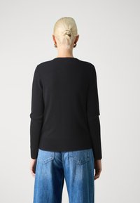 Maglione nero in maglia con scollatura rotonda e maniche lunghe, abbinato a jeans a gamba larga di colore blu chiaro con design a tasca sul retro.