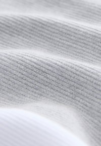 Szürke bordázott anyag lágy textúrával; finom vízszintes vonalakkal díszítve. Fehér anyagszegély látható a kép alsó részén.