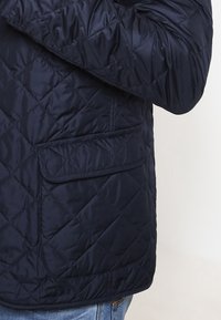 Navy gesteppte Jacke mit diagonaler Naht, einer rechteckigen Tasche und einer glatten, glänzenden Textur. Entwickelt für Wärme und Komfort.