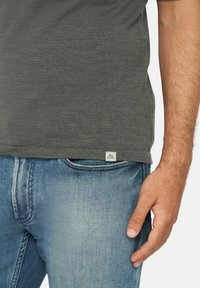 T-shirt grigio scuro a maniche corte con un tessuto testurizzato e un piccolo etichetta logo all'orlo, indossato con jeans in denim blu chiaro.