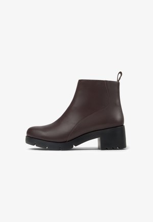 Bota de cuero marrón hasta el tobillo con tacón cuadrado, textura suave, punta redondeada y una lengüeta en la parte posterior; suela de goma con tracción antideslizante.