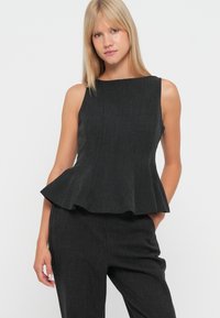 Melna pepluma blūze ar elegantu, strukturētu dizainu un teksturētu audumu. Piedurknes bez piedurknēm un apaļa kakla izgriezums noslēdz izskatu.