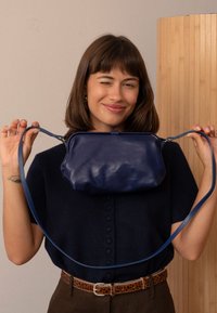 Borsa a tracolla in pelle blu navy con forma strutturata e texture liscia, caratterizzata da una lunga tracolla e una chiusura superiore.
