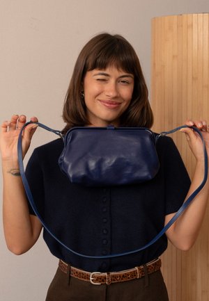 Borsa a tracolla in pelle blu navy con forma strutturata e texture liscia, caratterizzata da una lunga tracolla e una chiusura superiore.