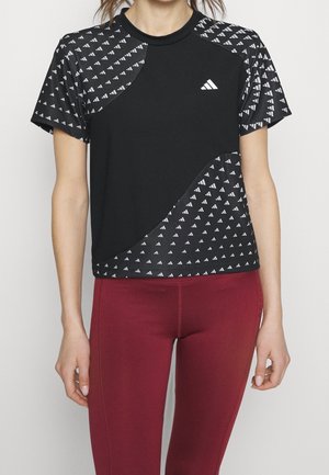 T-shirt de sport noir avec un motif géométrique blanc sur les manches et le bas du devant, présentant un col rond et un logo sur la poitrine.