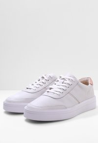 Baskets blanches avec une tige en cuir lisse, bout arrondi et accent métallique contrastant au talon. Elles disposent de lacets plats et d'une semelle épaisse.