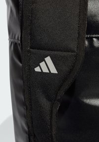 Black sports bag with a sleek, glossy material. Features a grey triangular logo and textured accents along the edges. Compact design.