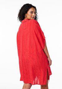 Röd, lätt crepe-tygklänning med lös passform, korta ärmar, krage och sidoklyftor. Strukturerade vertikala linjer överallt.