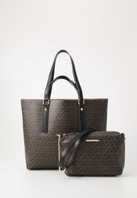 Brun mönstrad tygväska med svarta handtag och en matchande mindre väska. Båda är tillverkade av syntetiskt material med geometriska mönster.