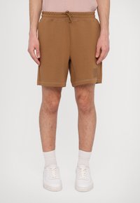 Brune bomullsshorts med elastisk midje og snor. Har en subtil logo og lette sømmer i kanten. Børt med hvite joggesko.