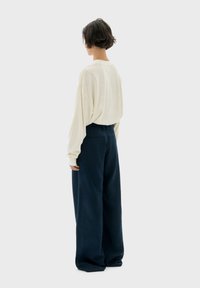 Camicia oversized crema a maniche lunghe e pantaloni blu navy a gamba larga, con trame morbide e vestibilità rilassata, vista da dietro su uno sfondo chiaro.