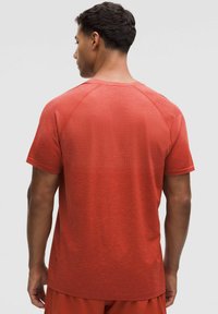 Punainen lyhythihainen urheilupaita, jossa on teksturoitu kangas ja raglan-hihat, pyöreä pääntie ja hieman kaareva helma.