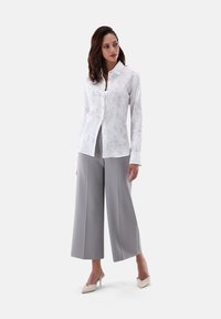Camicia bianca con texture floreale sottile, abbinata a pantaloni a gamba larga grigio chiaro e tacchi nudi. Design semplice e contemporaneo.