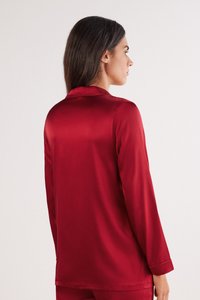Rød satinbluse med lange ærmer, krave og glat tekstur. Har en løs pasform, synlige sting og simple manchetter.
