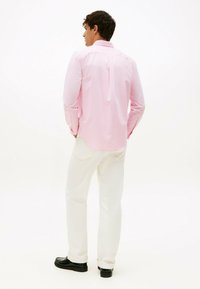 Lichtroze gestreepte overhemd met lange mouwen en een button-down kraag, gedragen met witte broek en zwarte schoenen. Achteraanzicht dat de pasvorm van het shirt benadrukt.