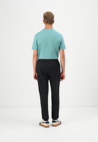 Απαλή τιρκουάζ κοντομάνικη μπλούζα, μαύρο παντελόνι με ελαστική μέση και λευκά αθλητικά παπούτσια με μαύρες ρίγες, με θέα από πίσω. Λείο υλικό.