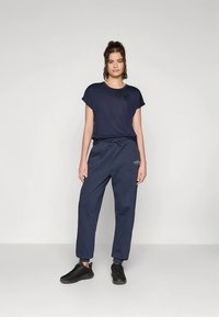 Donkerblauw T-shirt met korte mouwen gecombineerd met donkerblauwe joggingbroek met elastische tailleband en zijzakken, gedragen met zwarte sneakers.
