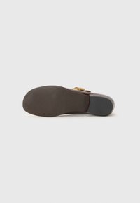 Sole di scarpa marrone lucida con un motivo di grip testurizzato, forma curva e una fibbia dorata sul lato. Materiale liscio e profilo piatto.