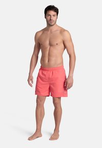 Pantaloni da bagno corallo con vita elastica, tasche laterali e fodera interna in rete. Presentano un delicato dettaglio del logo. Il tessuto sembra leggero.