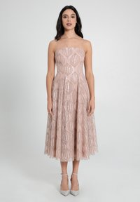 Ein ärmelloses A-Linien-Kleid in Hellpink mit einem strukturierten Muster aus erhabenen Blattformen. Der Stoff hat einen dezenten Glanz und ist mit silbernen Absätzen kombiniert.