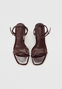 Dark burgundy strappy sandals with a glossy finish. Open-toed design, square toe shape, and thin ankle straps for secure fit.