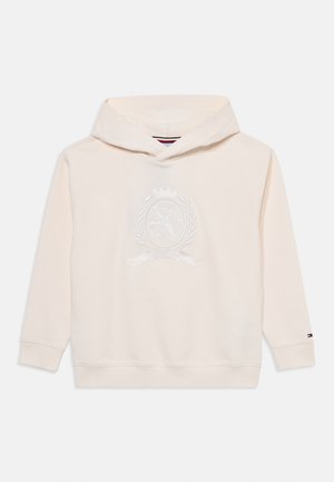 Crème-kleurige hoodie met kangoeroezak, geborduurd wapenontwerp in het midden, ribgebreide manchetten en zoom, met een logo-accent op de mouw.