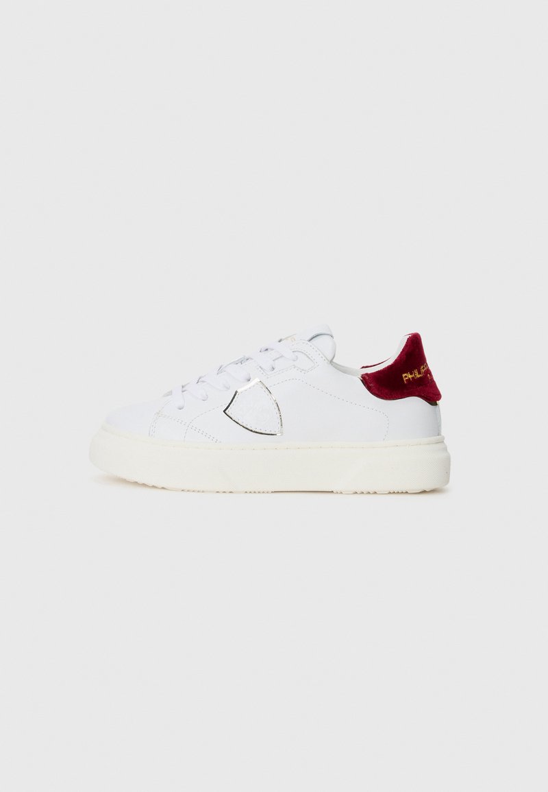 Weiße Sneaker mit einem glatten Lederobermaterial, metallisch silbernen Akzenten und einer burgunderroten Samt-Ferse. Dicke strukturierte Gummisohle.