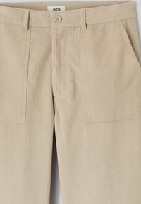 Pantalon en velours côtelé beige avec une surface texturée, doté d'une fermeture à bouton, de deux poches avant et d'un design soigneusement ajusté.