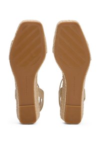 Sandales compensées beiges avec une semelle en espadrille, des brides en tissu texturé et une semelle en caoutchouc avec des rayures diagonales pour une meilleure adhérence.