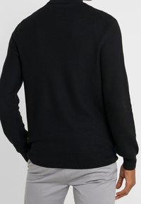 Svart stickad tröja med ett strukturerat mönster, ribbade muddar och nederkant. Designen har en rundad halsringning och en figurnära silhuett.