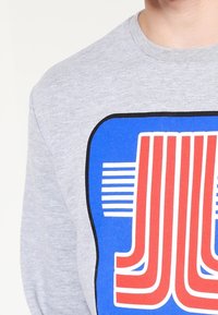 Sudadera gris con un diseño gráfico llamativo en azul y rojo, con rayas horizontales y una impresión similar a un logo en la parte frontal.